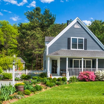 An American flag flies from the open porch and gardens surround a small single family home on a Spring afternoon on Cape Cod on the Massachusetts coast.